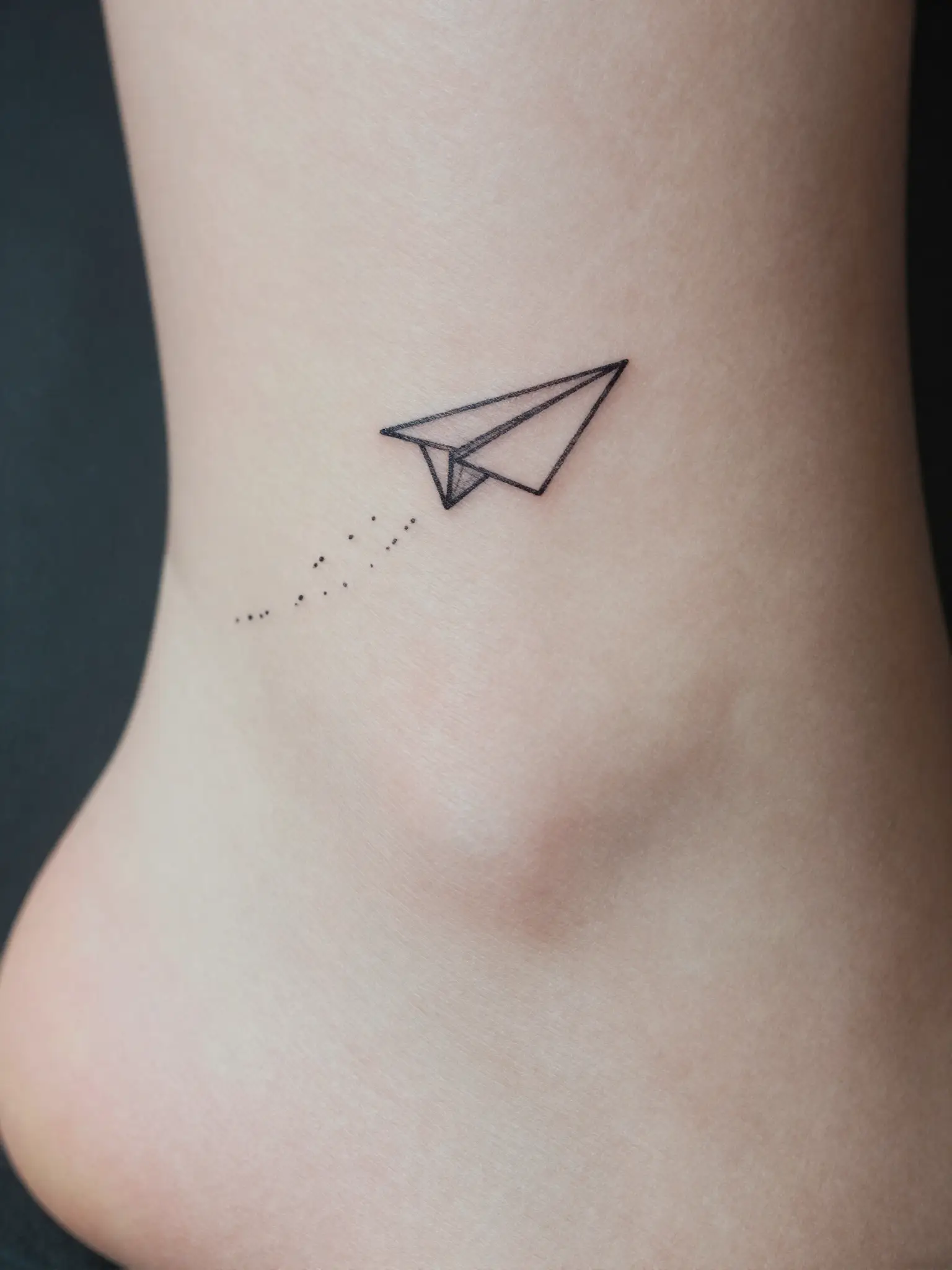 Tatuagem feminina de avião de papel pequeno em traço fino