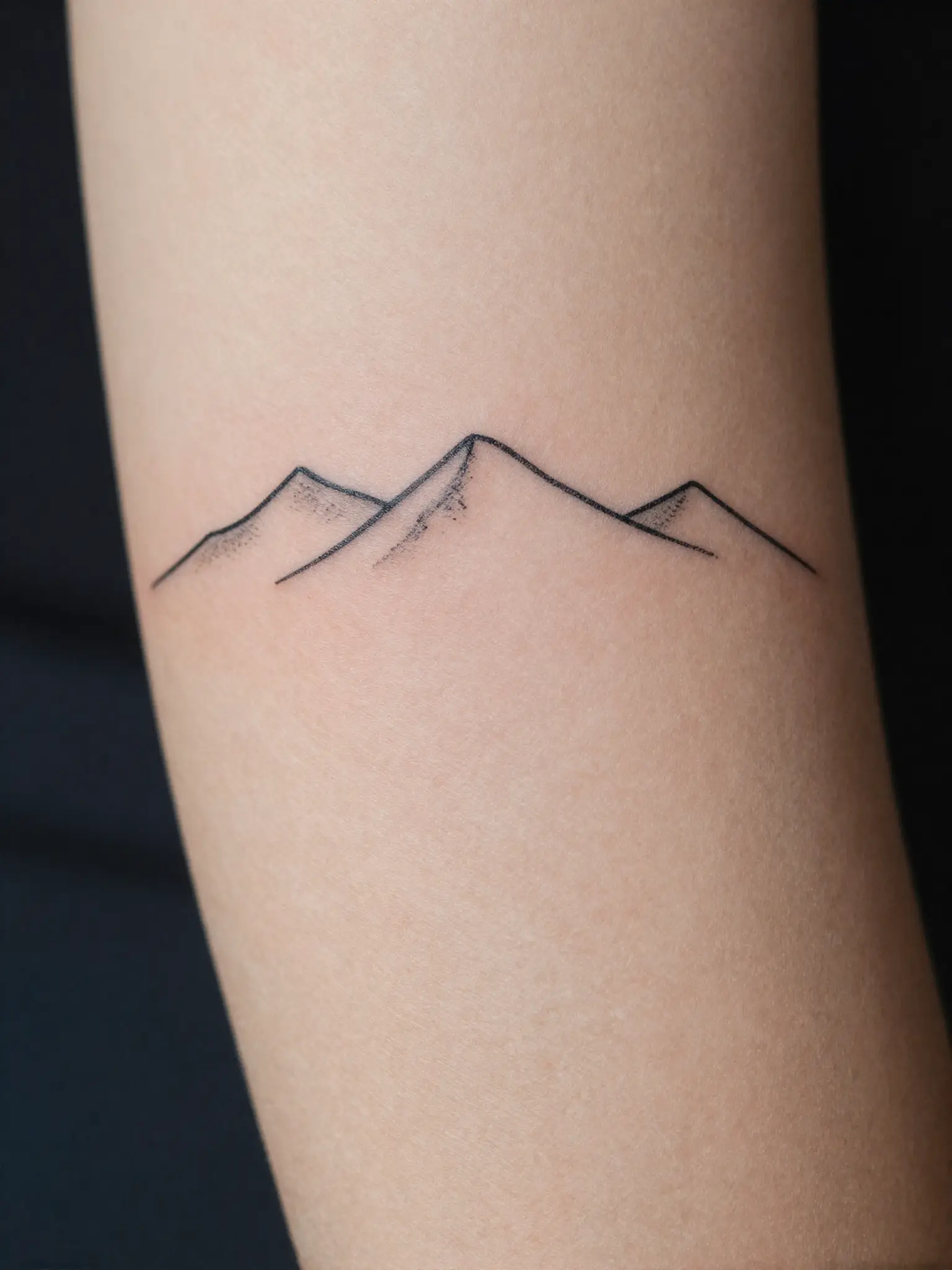 Tatuagem feminina de montanhas em traço fino no antebraço