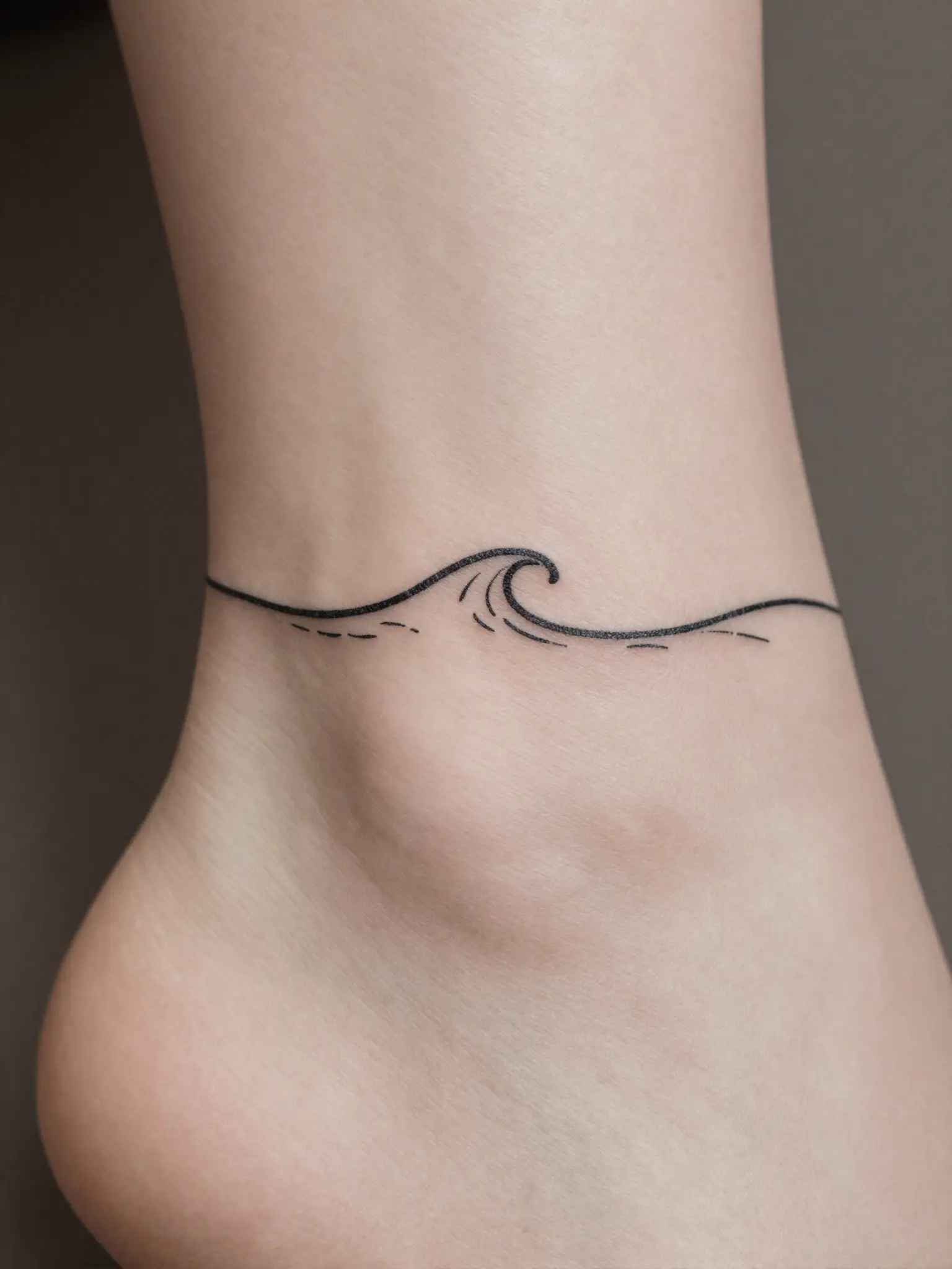 Tatuagem feminina de onda minimalista em traço fino no tornozelo