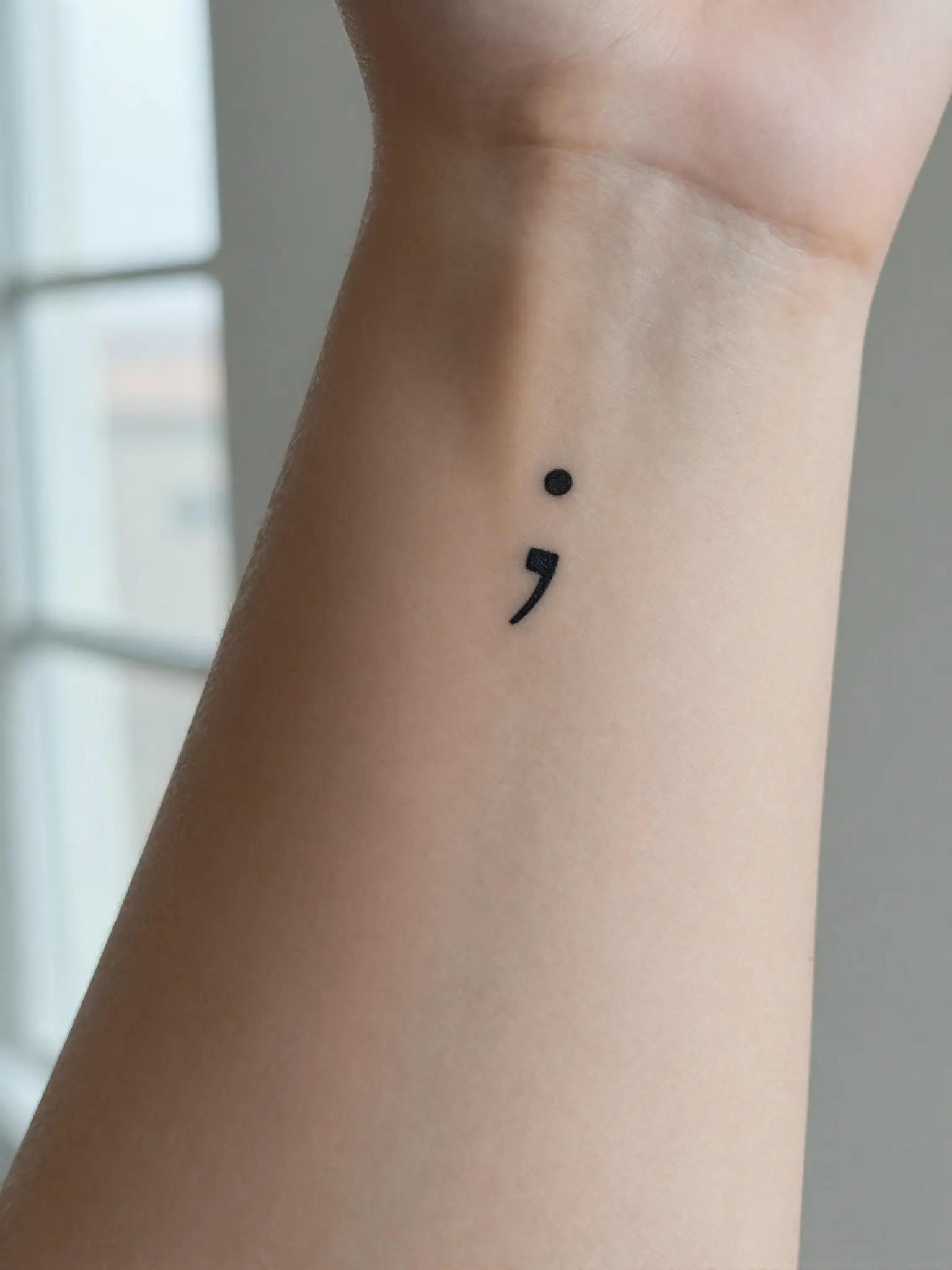 Tatuagem feminina de ponto e vírgula delicado no pulso