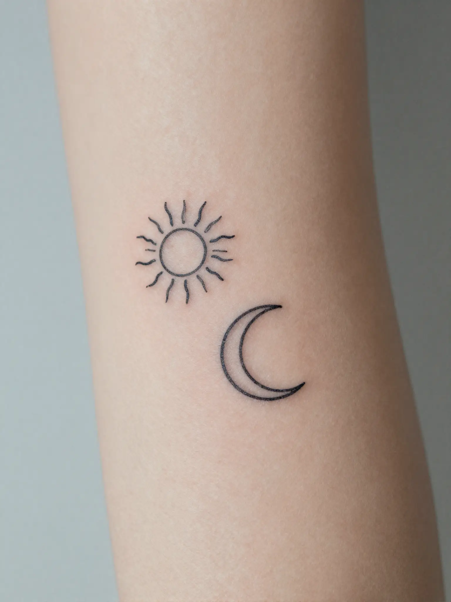 Tatuagem feminina de sol e lua minimalistas em traço fino